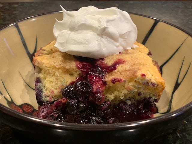 blueberry cobbler in a bowl with whip topping.