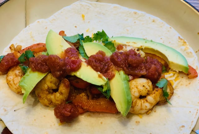 shrimp fajitas on a flour tortillas with avocado, salsa, cheese and cilantro.